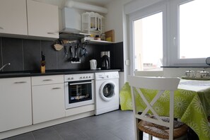 Une cuisine moderne avec des meubles blancs, un four encastré, un lave-linge et une machine à café.