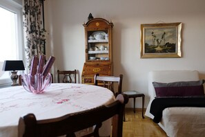A dining area with a table set for two, a wooden cabinet with dishes, a painting on the wall, and a bed with a purple pillow. - quiet accommodation in a central location 2km to Heidelberg (Leimen)