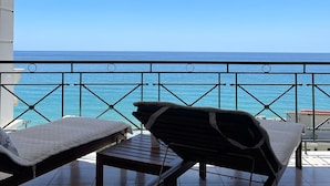 Ein Balkon mit zwei Liegestühlen, einem kleinen Tisch und Blick auf das Meer.