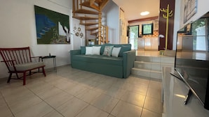 Ein geräumiger Wohnbereich mit einem grünen Sofa, einem Holzstuhl, einer Treppe und einer Küche im Hintergrund.