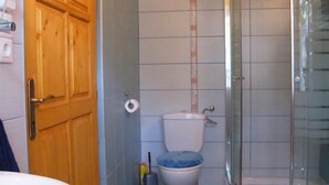Un baño con puerta de madera, inodoro con tapa azul, ducha con puerta de vidrio y lavamanos.