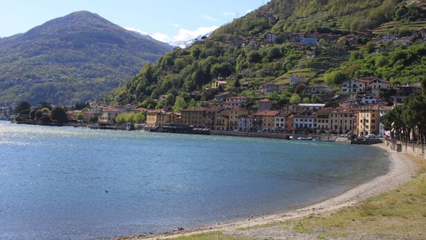 A lakeside town with buildings along the shore, a mountain in the background, and a clear sky.