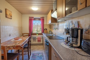 A compact kitchen with a dining area, wooden cabinets, a coffee maker, and a window with curtains.