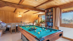 Et billardbord i et rum med trævægge og -loft, en reol og et vindue med udsigt.