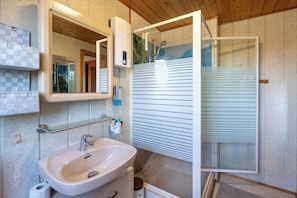 A bathroom with a sink, mirror, shower, and tiled walls.