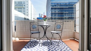 Un balcon avec une table et deux chaises, un pot de fleurs et une vue sur des immeubles modernes.