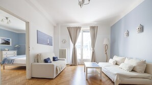 Une pièce spacieuse avec un parquet en bois disposé en motif chevron, un canapé blanc, un fauteuil blanc et une petite table blanche.