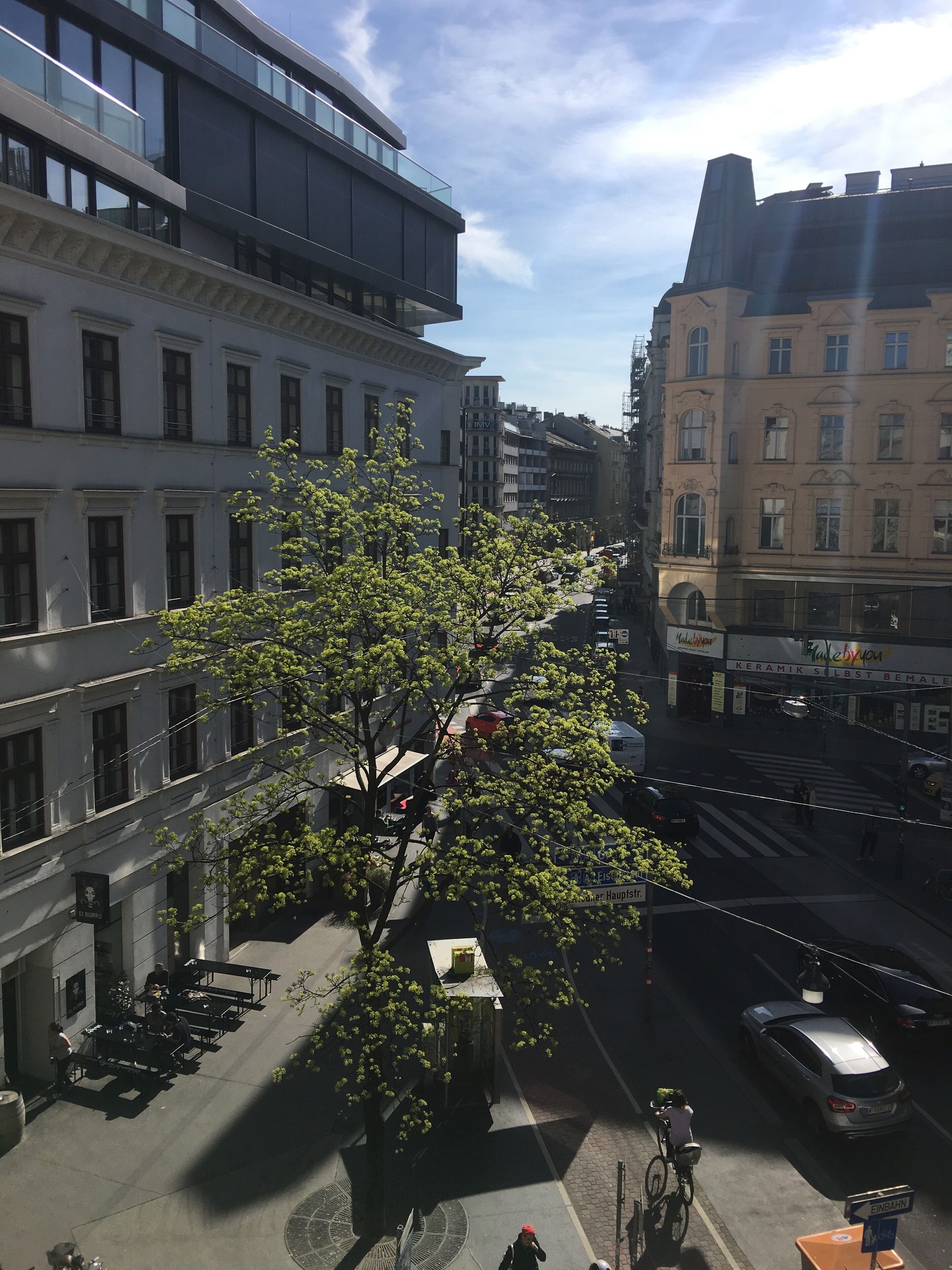 A street view with a tree-lined sidewalk, buildings with classical architecture, and a clear sky.
