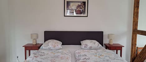 Un lit double avec une literie à motifs floraux, deux tables de chevet avec des lampes, une tête de lit en bois et un tableau encadré au mur.