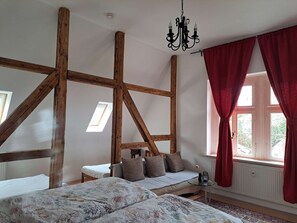 A room with exposed wooden beams, a bed with floral bedding, a small table, and a window with red curtains. - 1 Zimmer Appartment xxxxxxxxxxxxxxxxxxxx (Leichlingen)