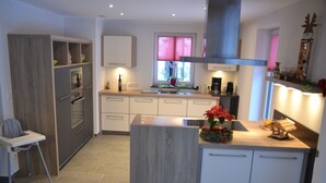 A modern kitchen with a central island, built-in appliances, and a window with pink blinds. - Eifelgold - Comfortable, spacious 5-star apartment in a quiet location  (Habscheid)
