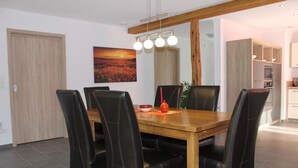 A dining area with a wooden table and black leather chairs, a painting on the wall, and a kitchen in the background. - Eifelgold - Comfortable, spacious 5-star apartment in a quiet location  (Habscheid)