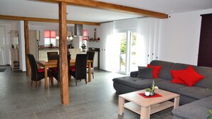 A spacious living area with a grey sofa, red cushions, and a wooden coffee table. A dining area with a wooden table and chairs is visible in the background. - Eifelgold - Comfortable, spacious 5-star apartment in a quiet location  (Habscheid)