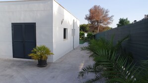 A modern building with a flat roof, a concrete courtyard, and a black metal fence. - Modern bungalow with heated pool, 50m from the sea - whirlpool - (Cala Pi)