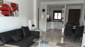 A modern living room with a sofa, a glass coffee table, and a dining area with chairs and a table. - Modern bungalow with heated pool, 50m from the sea - whirlpool - (Cala Pi)