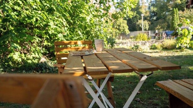 A wooden picnic table with a bench and a cup in a garden setting.