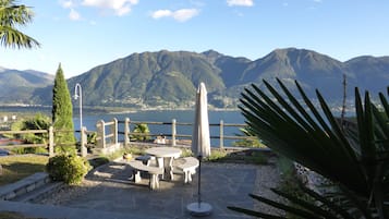 A patio with stone tables and chairs, a lamp post, and a view of mountains and a lake.