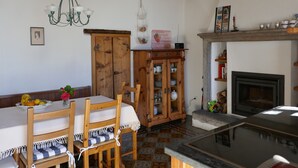 A rustic kitchen with wooden beams, a dining table with chairs, a cabinet with glass doors, and a fireplace.