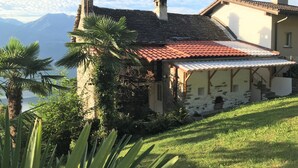 A stone building with a red-tiled roof, a covered porch, and a view of mountains in the background.