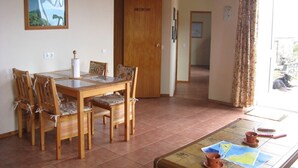 Un comedor con una mesa y sillas de madera, una lámpara en el techo y vistas al exterior a través de una ventana con cortinas.