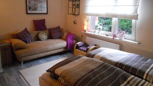Ein gemütliches Zimmer mit einer Couch, zwei Betten, einem Fenster mit Blick, einem Heizkörper und einem gerahmten Bild an der Wand.