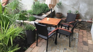 A patio area with a wooden table and four wicker chairs, surrounded by potted plants and a stone wall. - Quiet living in the heart of Görlitz in elegant style (Görlitz)