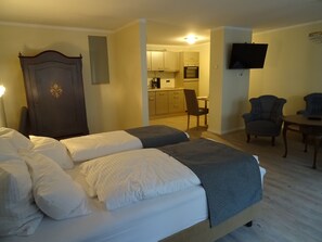 A hotel room with two beds, a desk, a chair, a TV, and a kitchenette.