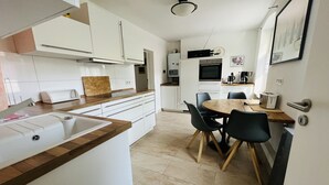 A modern kitchen with white cabinets, a wooden countertop, a sink, and a dining area with chairs and a table. - Welcome to the Oderbruch (Wriezen)
