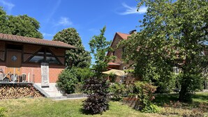 A brick building with a red-tiled roof, a small garden with various plants, and a clear blue sky. - Welcome to the Oderbruch (Wriezen)