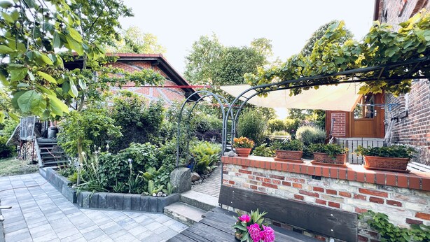 A patio area with a brick wall, a wooden bench, and potted plants. - Welcome to the Oderbruch (Wriezen)