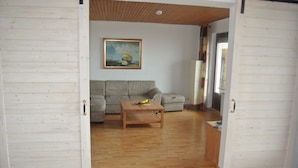 Un salon avec un plancher en bois, un canapé gris, une table basse en bois sur laquelle sont disposés des fruits, et un tableau accroché au mur.