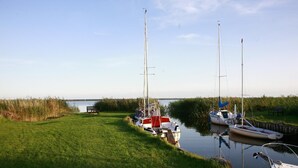 A calm waterway with boats docked, grassy banks, and a distant view of a body of water.