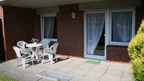 Un patio con mesa y sillas, un pequeño jardín y un edificio de ladrillo con dos ventanas.