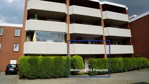 Un edificio residencial de varios pisos con balcones, fachada de ladrillo y zona de estacionamiento.