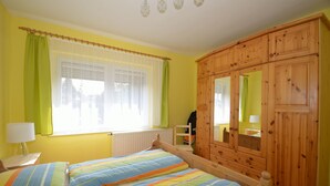 Un dormitorio con dos camas, un armario de madera, una ventana con cortinas y un radiador.