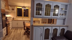A compact kitchen with white cabinetry, a dining area with a table and chairs, and a black leather sofa.