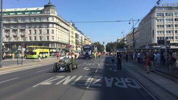 Eine Straße mit einer Straßenbahn, einem Oldtimer und einer Menschenmenge.