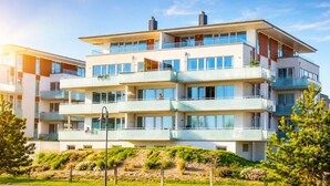 Un immeuble résidentiel à plusieurs étages, doté de balcons, de grandes fenêtres et d’un jardin paysager à l’avant.