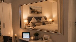 Une chambre à coucher comprenant un lit, des lampes de chevet, une horloge numérique, un miroir et une petite table ornée d’objets décoratifs.