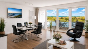 Un salon moderne comprenant un coin repas, de grandes portes-fenêtres coulissantes donnant sur une terrasse et une vue sur un paysage côtier.