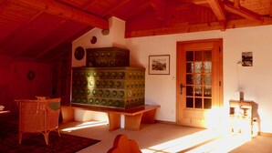A room with a wooden ceiling, a green chest of drawers, a wicker chair, a bench, and a door with a window.