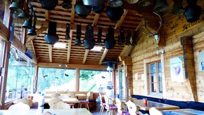 A rustic wooden interior with multiple tables and chairs, wooden beams on the ceiling, and a view through the windows.
