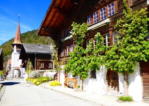Un bâtiment traditionnel en bois, doté d’un toit à forte pente, d’un petit clocher et d’un balcon orné de plantes grimpantes.