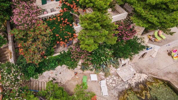 An aerial view of a house with a stone facade, green shutters, and a garden with flowering plants. - Villa located directly at the sea (Klek)