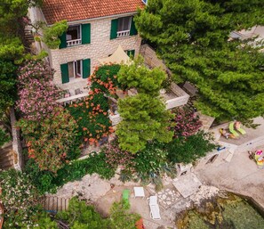 An aerial view of a house with a stone facade, green shutters, and a garden with flowering plants.