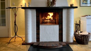 A fireplace with a fire, a mantel with decorative items, and a standing lamp. - Large cozy apartment centrally in Winterberg with panoramic views (Winterberg)