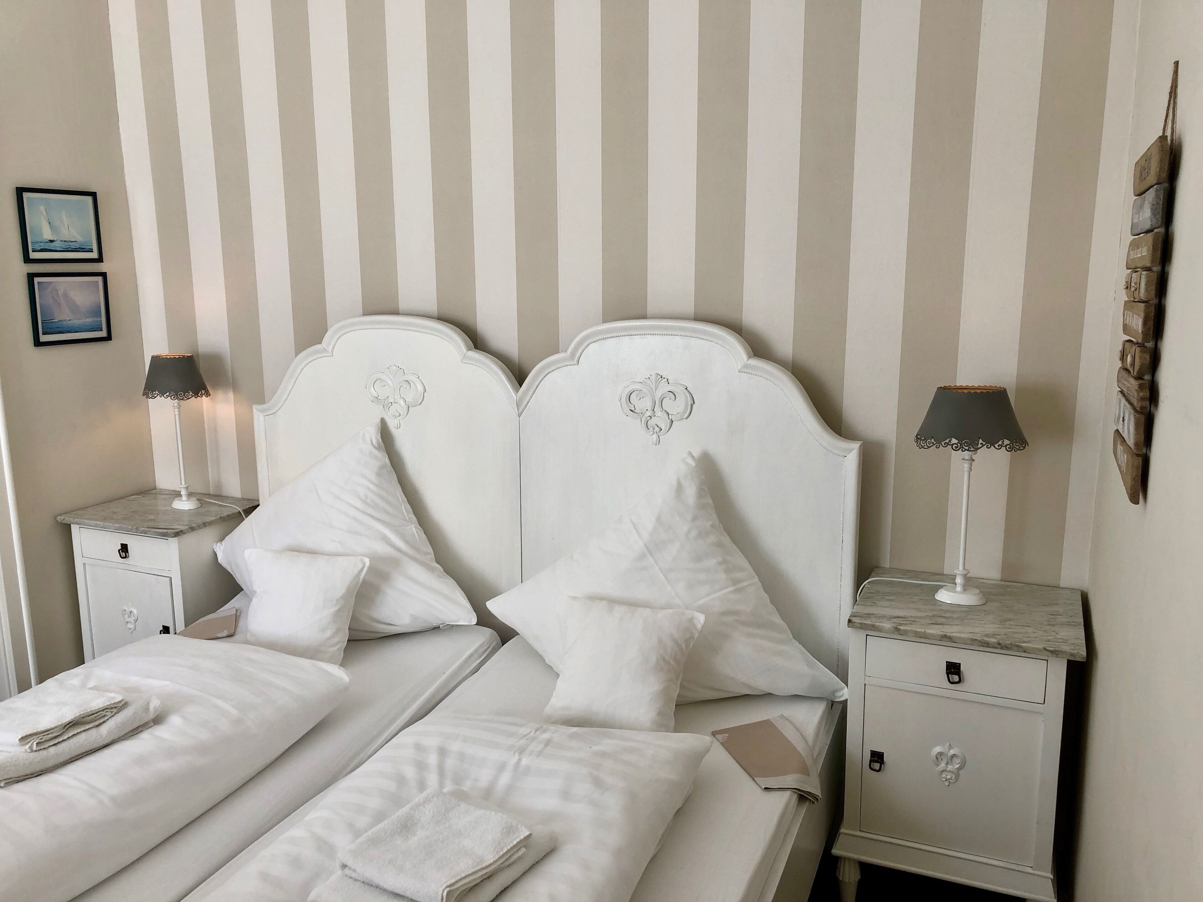 A neatly made bed with white linens and pillows, two bedside tables with lamps, and a striped wall.