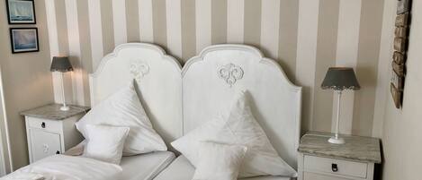 A neatly made bed with white linens and pillows, two bedside tables with lamps, and a striped wall.