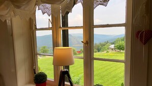 A room with a window overlooking a green landscape, a lamp on a tripod stand, and two potted plants on the windowsill. - Large cozy apartment centrally in Winterberg with panoramic views (Winterberg)