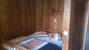 A wooden room with a bed, a wooden headboard, and a small window.